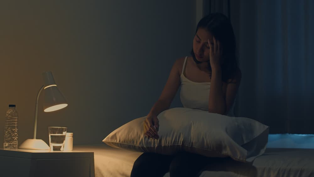 Woman suffering from insomnia sits up in bed